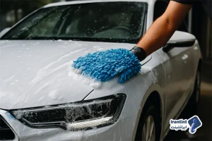 شست‌وشوی بدنه یک خودروی سفید با دستکش میکروفایبر آبی و کف فراوان در حال تمیزکاری